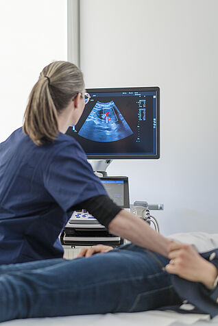 Die Abbildung zeigt eine Untersucherin bei der Ultraschalluntersuchung eines Probanden auf der Liege.